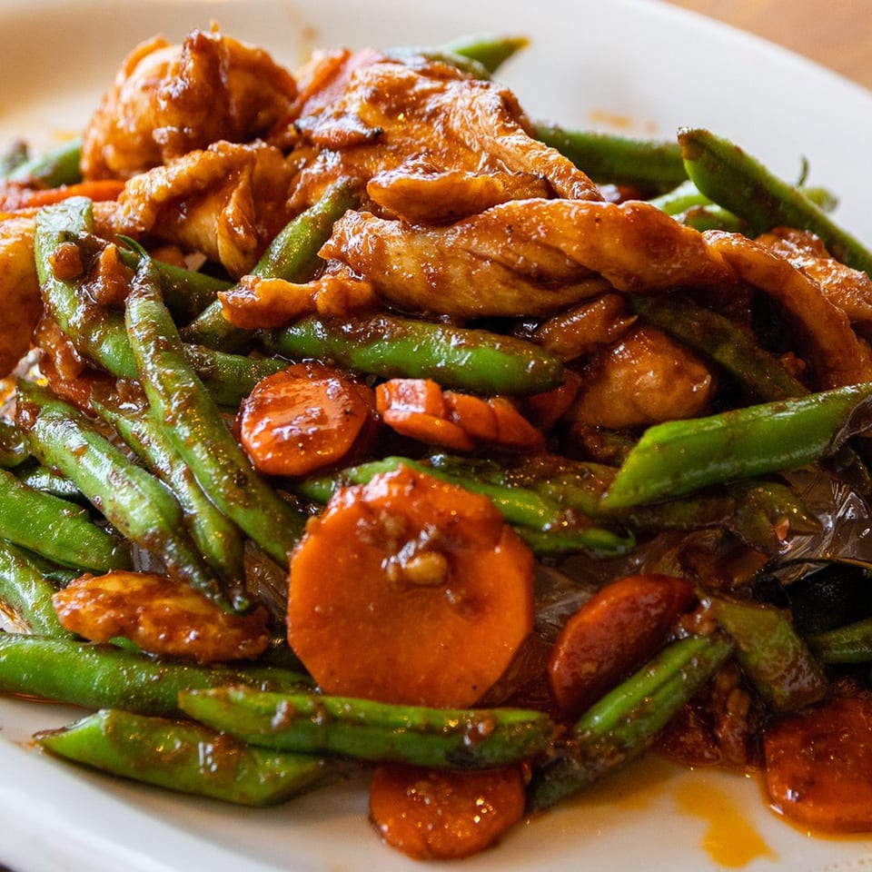 Peppers Thai chicken stir-fry with green beans and carrots in a savory sauce.
