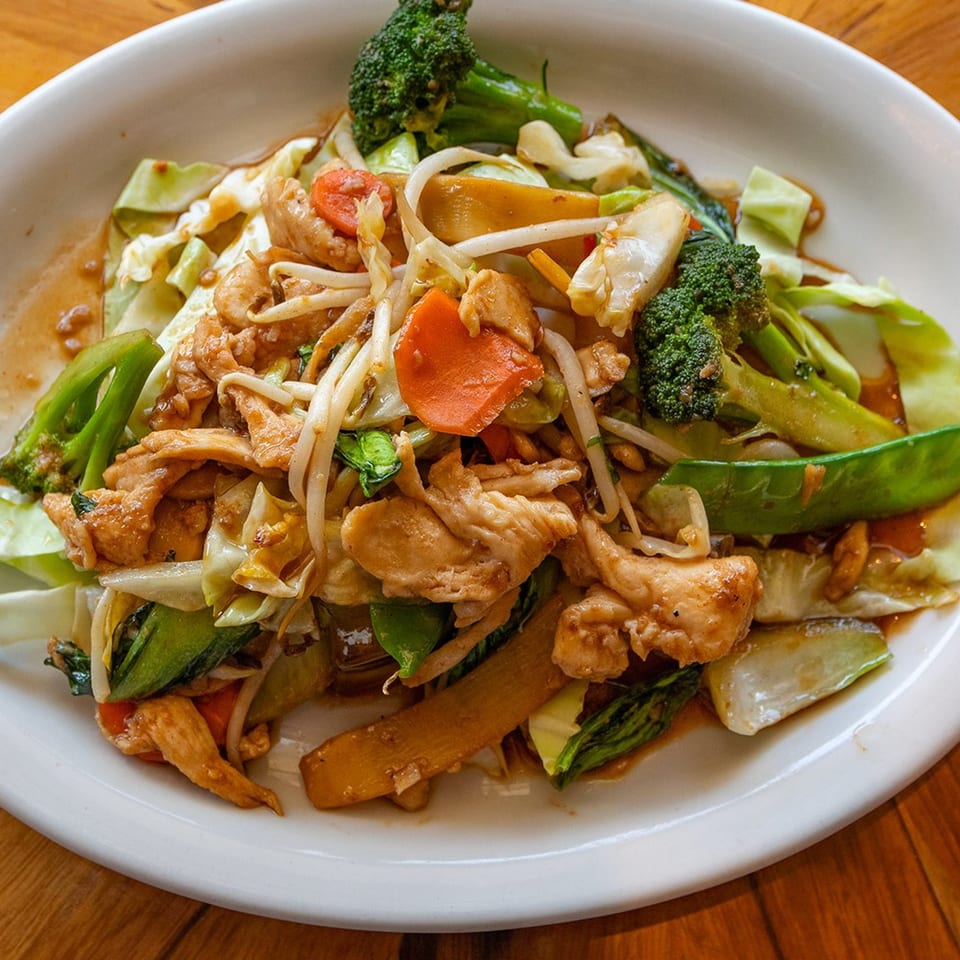 A white plate filled with Peppers Thai stir-fried chicken and mixed vegetables in a savory sauce.