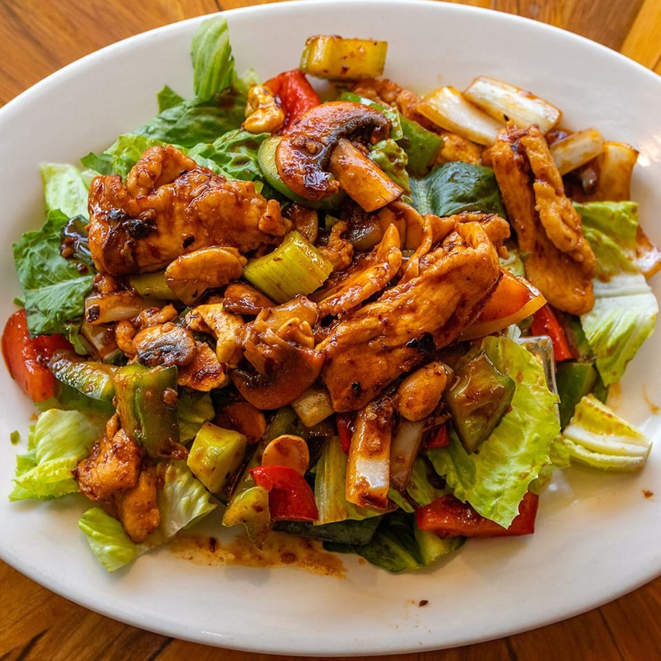 Peppers Thai chicken stir-fry with mushrooms, bell peppers, and onions on a bed of lettuce.